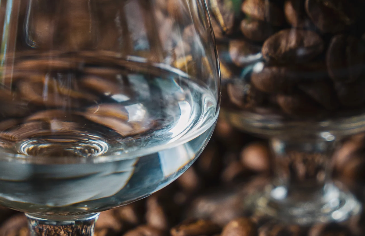 Grains de café fraîchement torréfiés et verre de spiritueux au café illustrant le travail aromatique de la Distillerie Sainte Barbe.